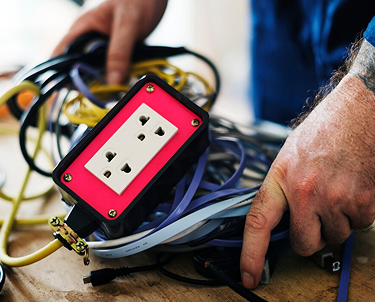 Close-up of hands sorting through a tangled mess of various electrical wires and a multi-socket extension cord.