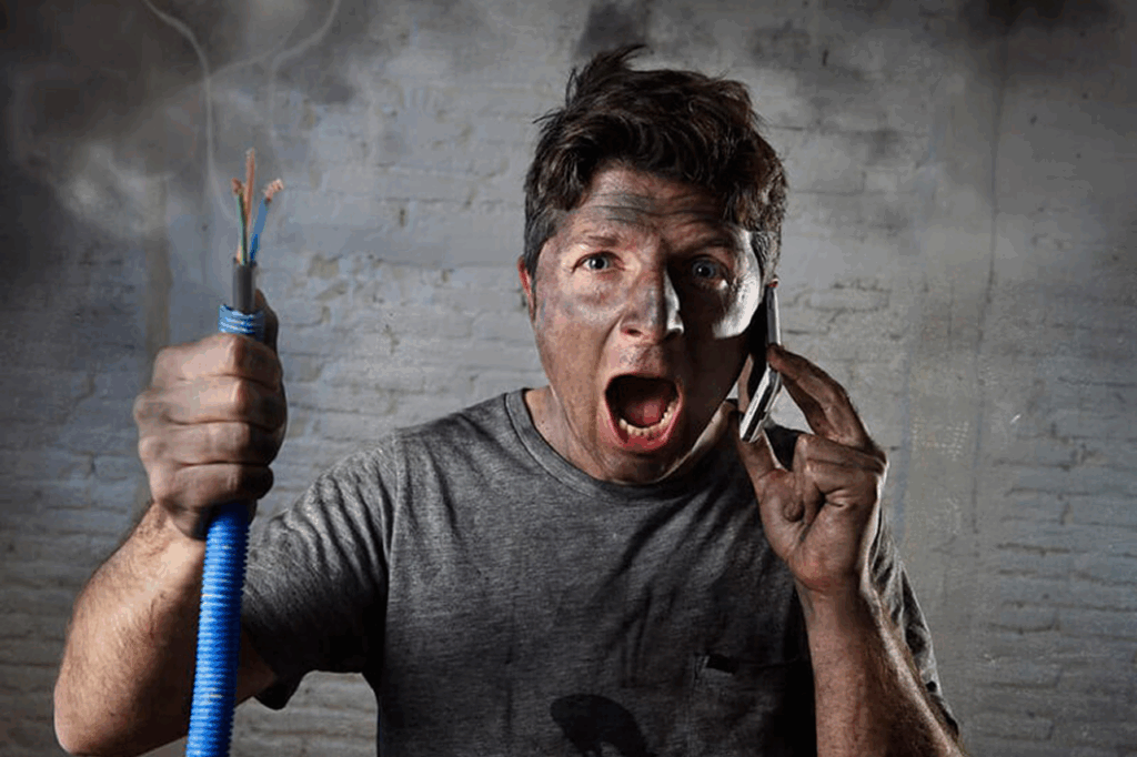 Person with soot-covered face and singed electrical wire urgently calling on a cell phone. Emergency Electrical Services