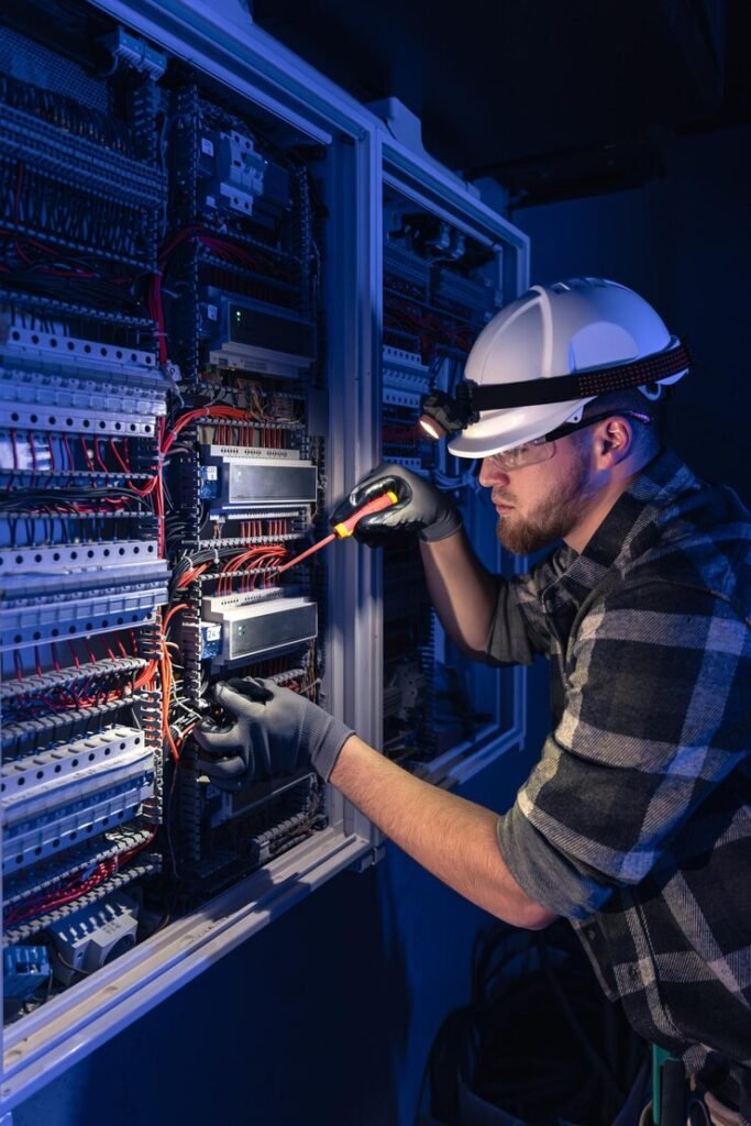 Male electrician in overalls working on a switchboard with emergency lighting in the background